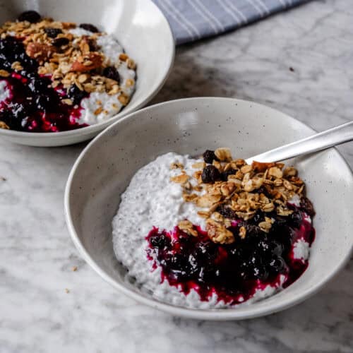 Alt-tekst: Yoghurt med bær, granola og nødder i to skåle på marmorbord.